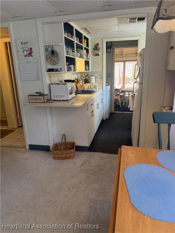 kitchen with white appliances, a drop ceiling, white cabinets, a sink, and visible vents
