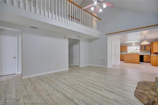 unfurnished living room with light wood-type flooring, a towering ceiling, and ceiling fan