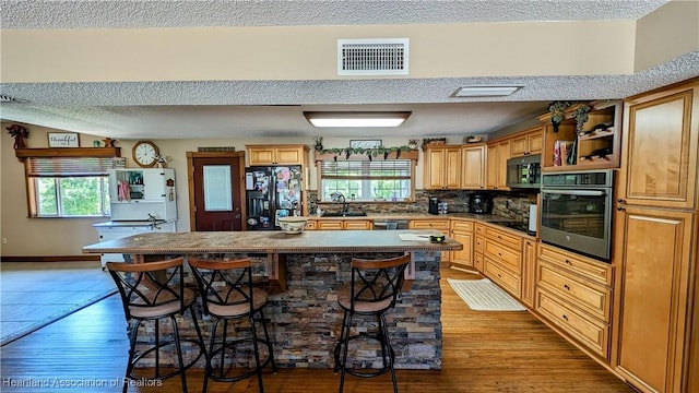 kitchen featuring light wood-type flooring, a breakfast bar, sink, black appliances, and a kitchen island