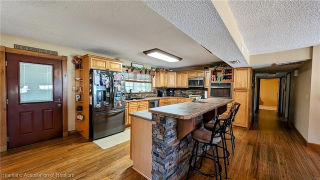 kitchen featuring a textured ceiling, a center island, hardwood / wood-style flooring, and black appliances