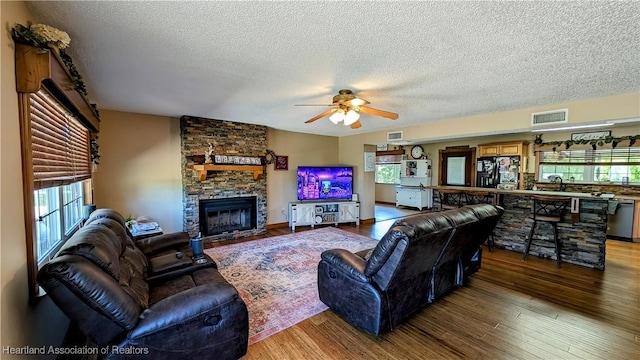 living room with a stone fireplace, sink, hardwood / wood-style flooring, ceiling fan, and a textured ceiling