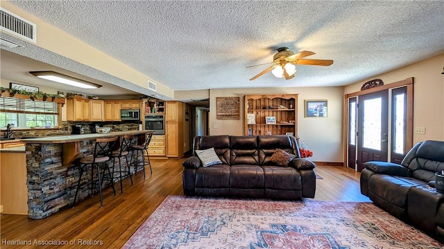 living room with a textured ceiling, dark hardwood / wood-style flooring, and ceiling fan