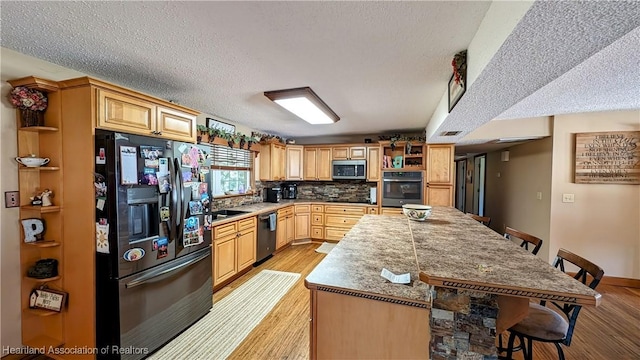 kitchen featuring backsplash, light wood-type flooring, light brown cabinetry, a kitchen bar, and stainless steel appliances