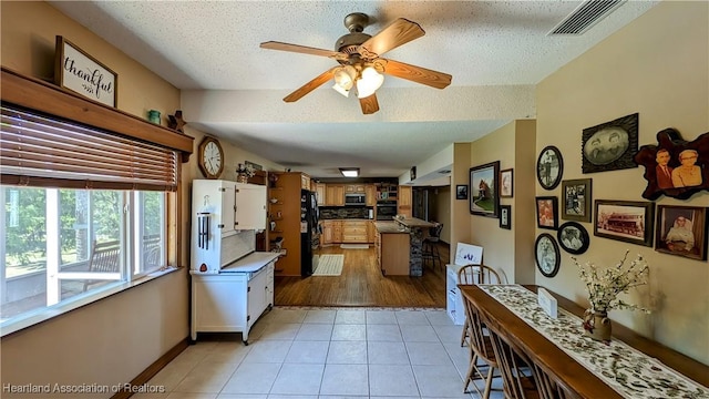 kitchen with black refrigerator, light tile patterned floors, a textured ceiling, and white cabinetry