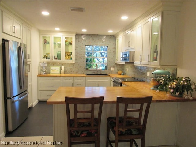 kitchen featuring wooden counters, appliances with stainless steel finishes, kitchen peninsula, sink, and white cabinetry