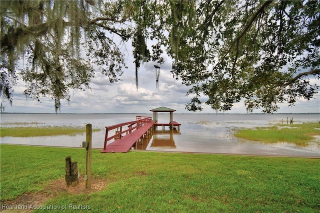 view of dock with a water view and a lawn