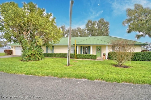 ranch-style home with a garage, metal roof, a front lawn, and stucco siding