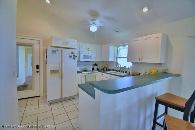 kitchen with dark countertops, white cabinets, a sink, white appliances, and a peninsula