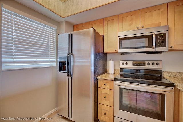 kitchen featuring appliances with stainless steel finishes, light stone counters, baseboards, and light brown cabinetry