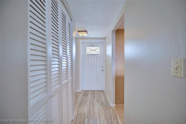 hallway with a textured ceiling, baseboards, and light wood-style floors