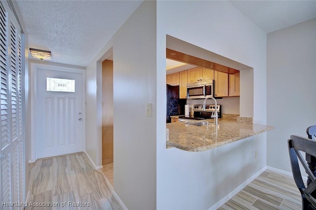 kitchen featuring light stone counters, a breakfast bar, stainless steel appliances, a textured ceiling, and baseboards