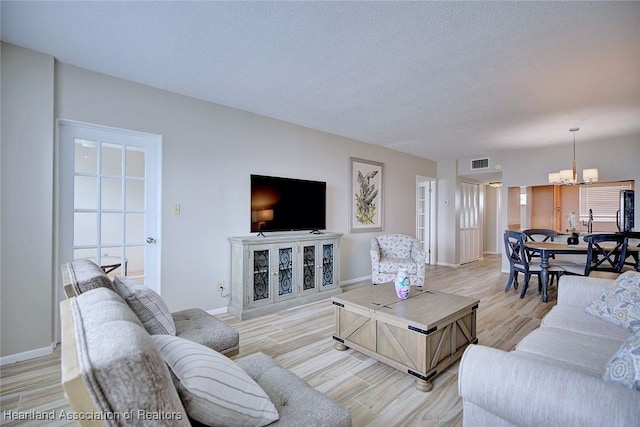 living area with baseboards, visible vents, a textured ceiling, and light wood finished floors