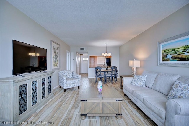 living room with baseboards, visible vents, a textured ceiling, wood finish floors, and a notable chandelier