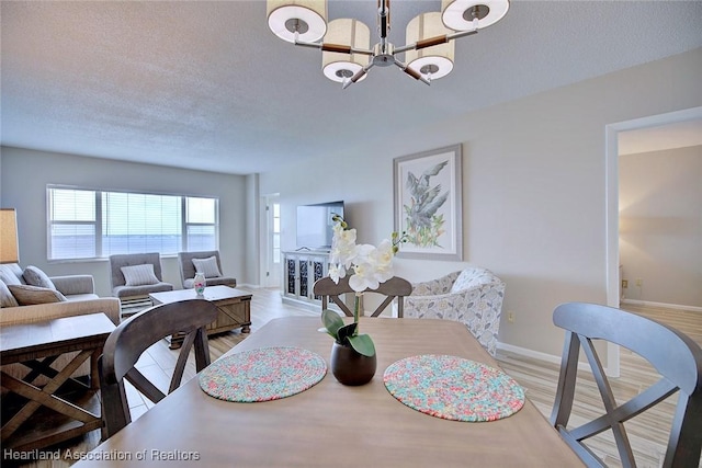 dining room featuring a textured ceiling, a notable chandelier, wood finished floors, and baseboards