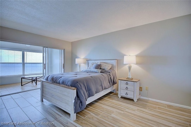 bedroom with light wood finished floors, baseboards, and a textured ceiling