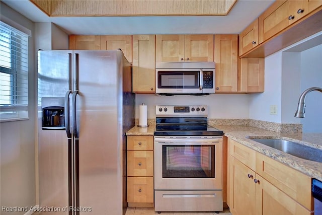 kitchen with stainless steel appliances, light brown cabinets, a sink, and light stone countertops