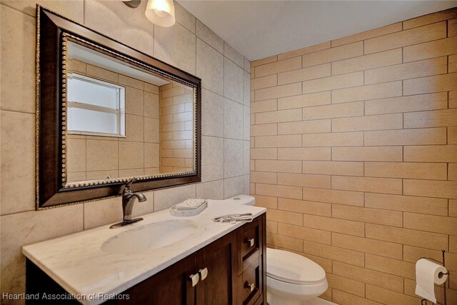 half bath with toilet, tile walls, and vanity