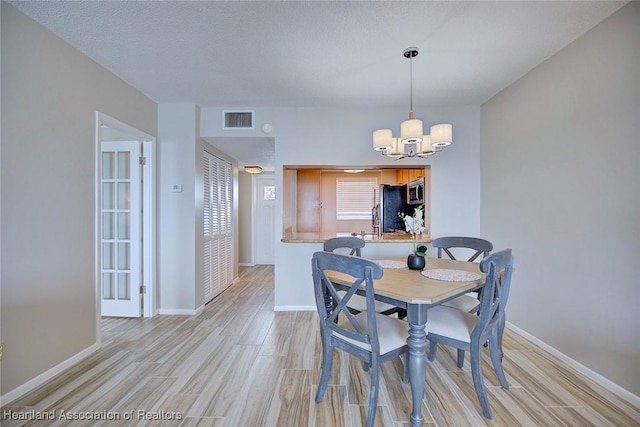 dining space featuring light wood-type flooring, baseboards, visible vents, and a notable chandelier