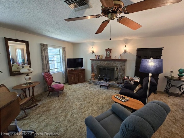 living room with ceiling fan, carpet flooring, a stone fireplace, and a textured ceiling