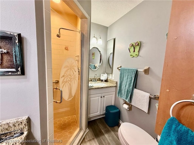 full bath featuring toilet, a stall shower, vanity, a textured ceiling, and wood finished floors