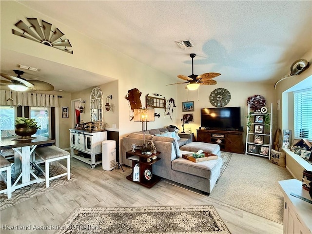 living area with a textured ceiling, ceiling fan, light wood-type flooring, and visible vents