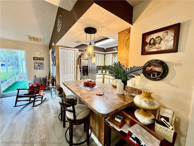 kitchen featuring pendant lighting, stainless steel refrigerator with ice dispenser, visible vents, wood finished floors, and a kitchen bar