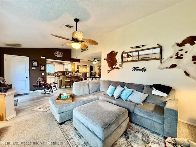 living area with lofted ceiling, visible vents, a textured ceiling, and light wood finished floors