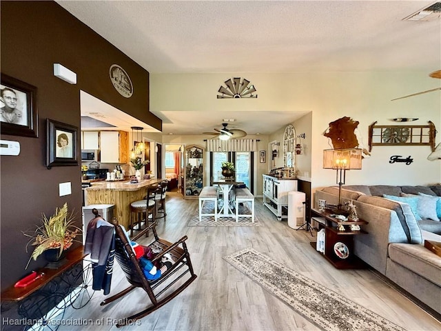 living area featuring light wood-style flooring, a textured ceiling, visible vents, and a ceiling fan