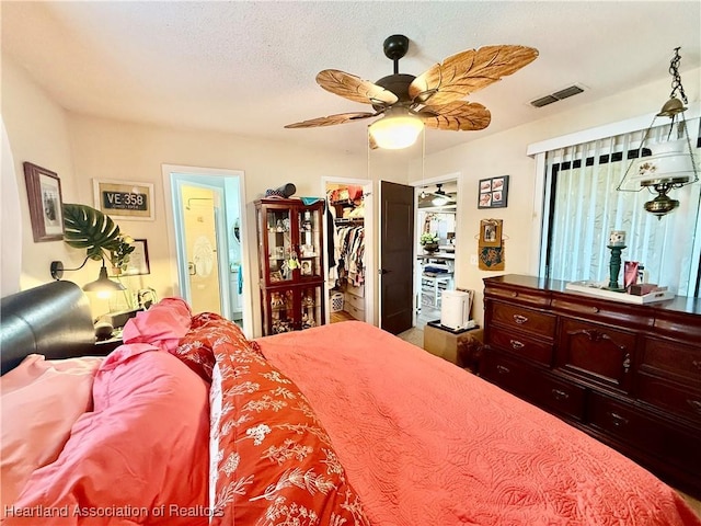 bedroom with a textured ceiling, connected bathroom, a ceiling fan, visible vents, and a walk in closet