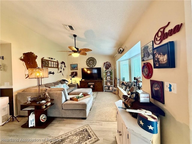 living area with lofted ceiling, a textured ceiling, visible vents, a ceiling fan, and light wood-type flooring