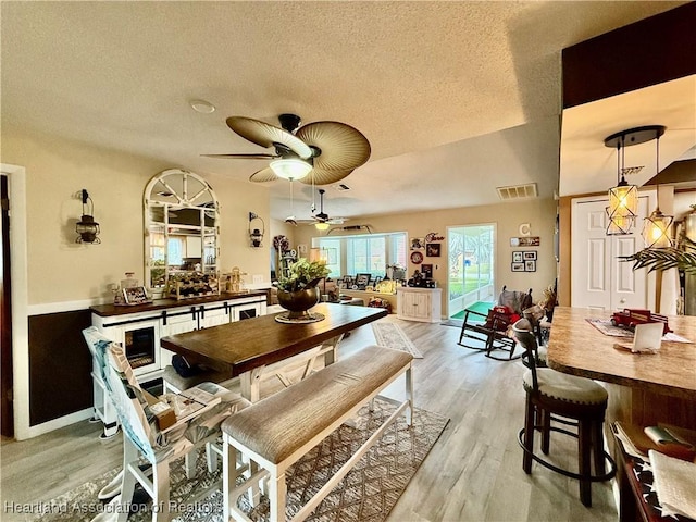 dining space featuring light wood finished floors, a ceiling fan, visible vents, and a textured ceiling