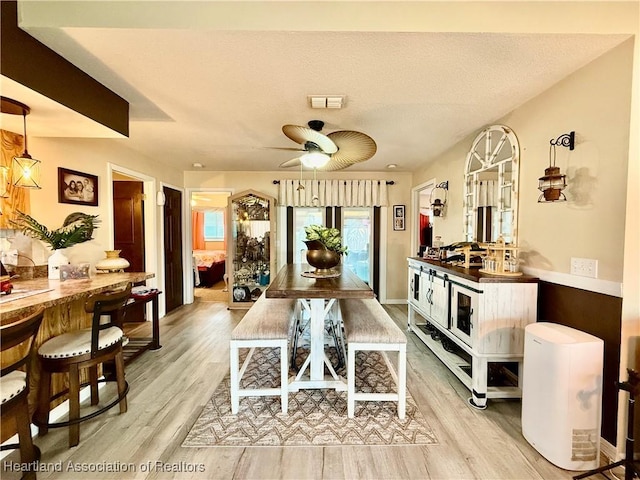 dining space with a ceiling fan, light wood-type flooring, visible vents, and a textured ceiling