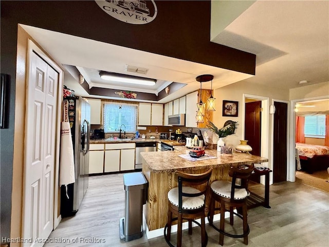 kitchen featuring light wood finished floors, a raised ceiling, appliances with stainless steel finishes, a peninsula, and white cabinetry