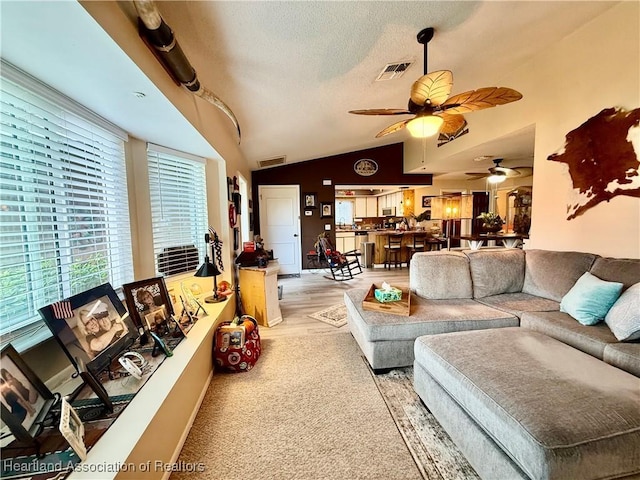 living area with a ceiling fan, visible vents, vaulted ceiling, and a textured ceiling