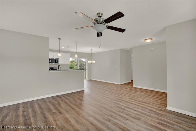 unfurnished living room featuring hardwood / wood-style floors and ceiling fan with notable chandelier