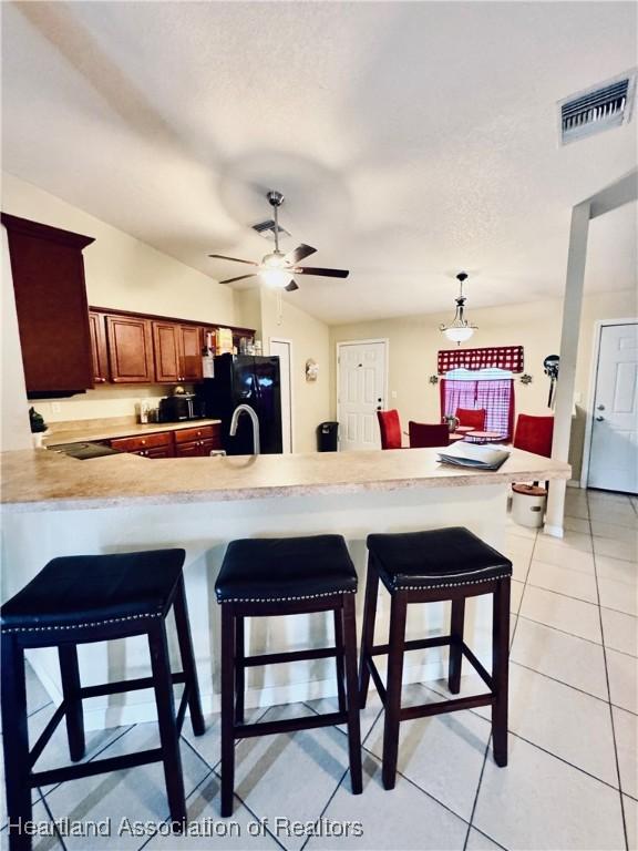 kitchen featuring pendant lighting, a breakfast bar area, light tile patterned floors, black fridge with ice dispenser, and kitchen peninsula