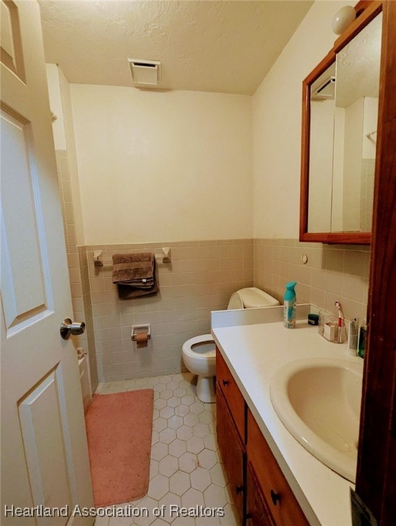 bathroom featuring tile patterned flooring, a textured ceiling, toilet, vanity, and tile walls