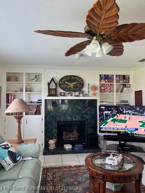 tiled living room with a fireplace, a textured ceiling, ceiling fan, and ornamental molding