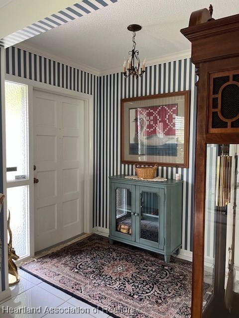 tiled entrance foyer featuring a chandelier, a textured ceiling, and crown molding