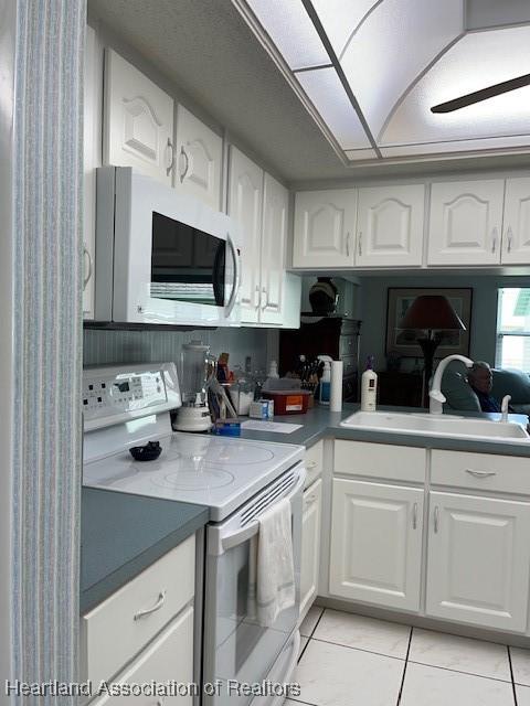 kitchen featuring white cabinets, white appliances, sink, and light tile patterned floors