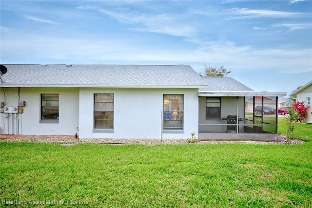 back of house featuring a sunroom, roof with shingles, a yard, and stucco siding