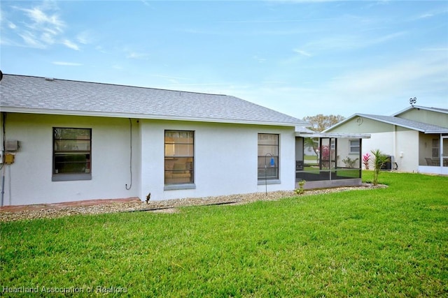 back of property featuring roof with shingles, a lawn, and stucco siding