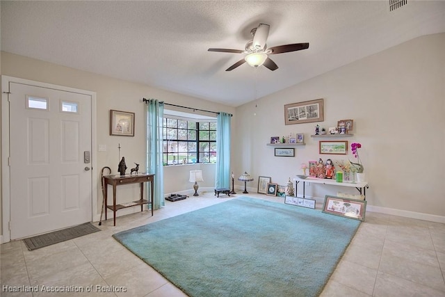 foyer with lofted ceiling, light tile patterned floors, ceiling fan, and a textured ceiling