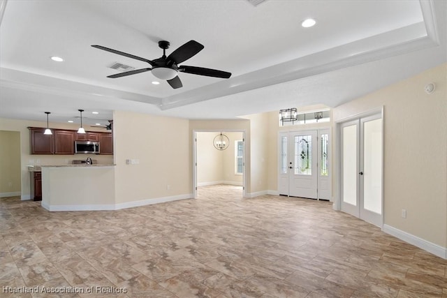 unfurnished living room with a tray ceiling and ceiling fan with notable chandelier