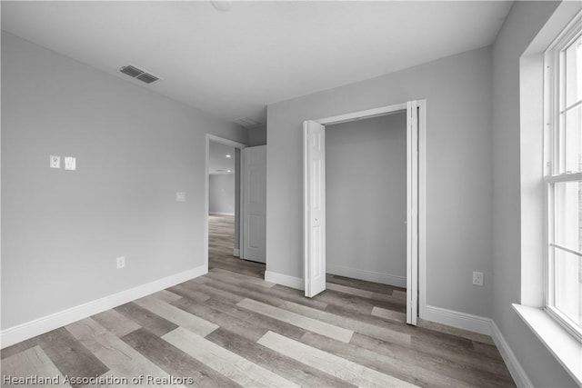 unfurnished bedroom with a closet, light wood-type flooring, and multiple windows