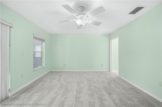 carpeted empty room with baseboards, visible vents, and a ceiling fan