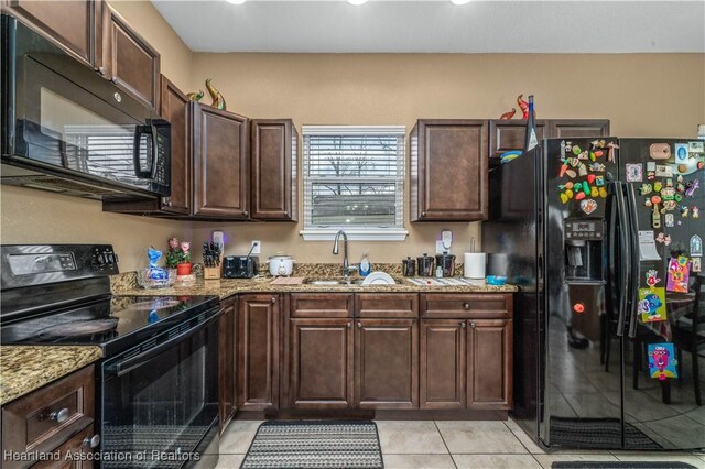 kitchen featuring light stone countertops, dark brown cabinets, sink, black appliances, and light tile patterned flooring