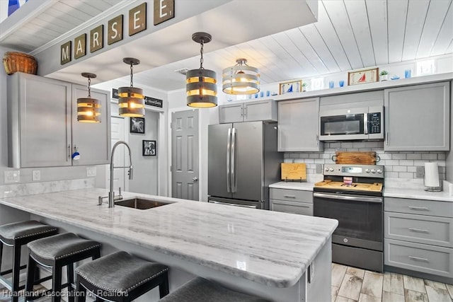 kitchen featuring gray cabinetry, stainless steel appliances, a peninsula, a sink, and backsplash