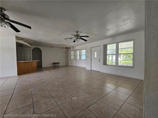 unfurnished living room with a textured ceiling, ceiling fan, ornamental molding, and light tile patterned flooring