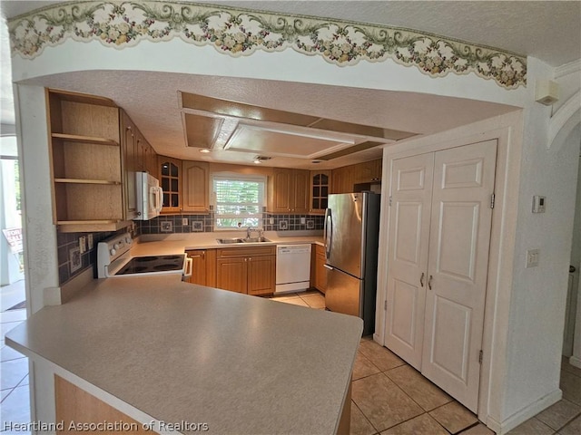 kitchen with kitchen peninsula, white appliances, a tray ceiling, sink, and light tile patterned floors